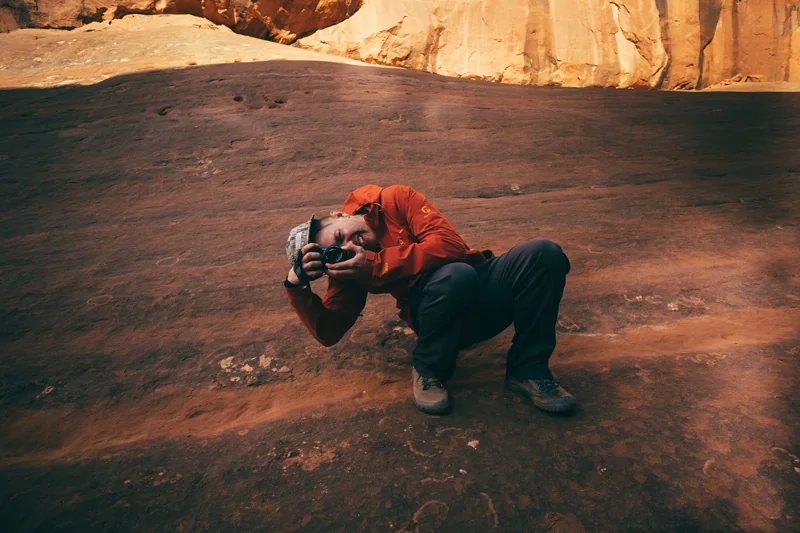 Brian crouching with a camera on red sandstone